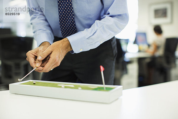 Geschäftsmann spielt mit Spielzeuggolf im Büro