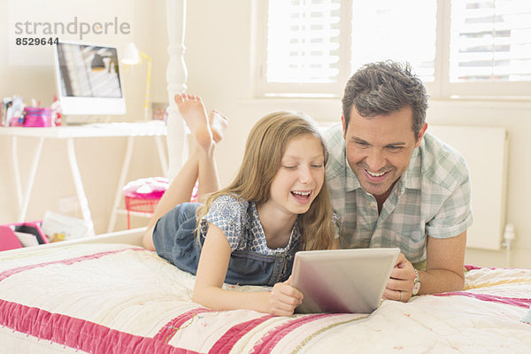 Vater und Tochter mit digitalem Tablett auf dem Bett