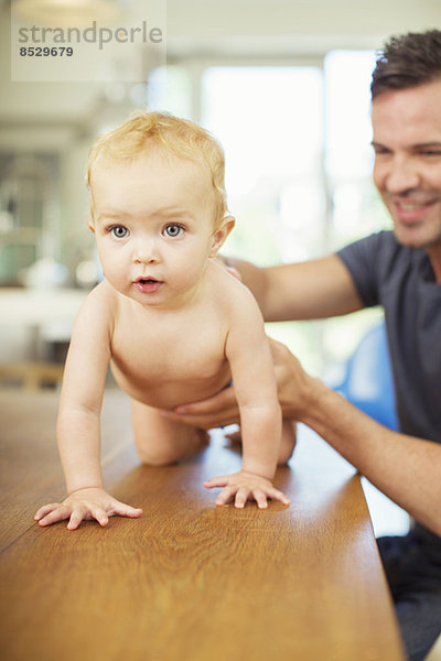 Vater hilft Baby auf dem Tisch krabbeln