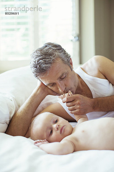 Vater küsst Babys Hand auf dem Bett