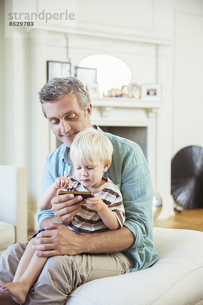 Vater und Sohn mit dem Handy im Wohnzimmer