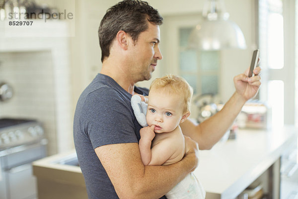 Vater benutzt Handy und hält Baby.