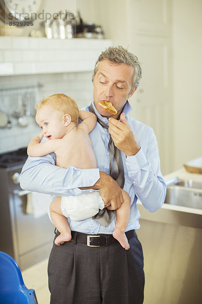 Vater hält Baby und isst Frühstück