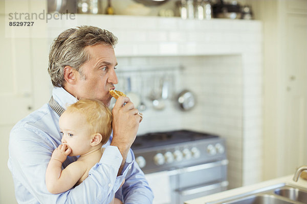 Vater hält Baby und isst Frühstück