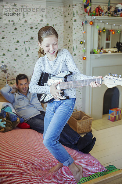 Mädchen spielt Gitarre für Vater im Schlafzimmer