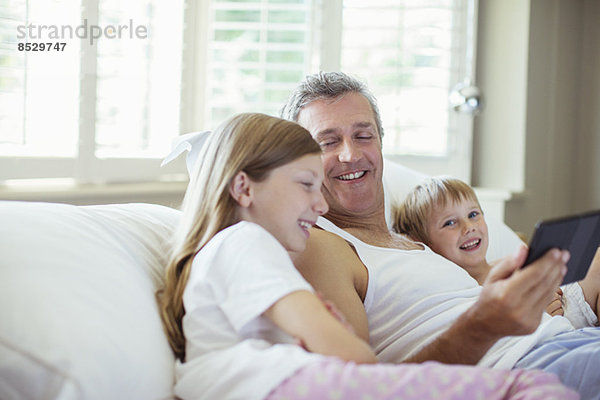 Vater und Kinder mit digitalem Tablett im Bett