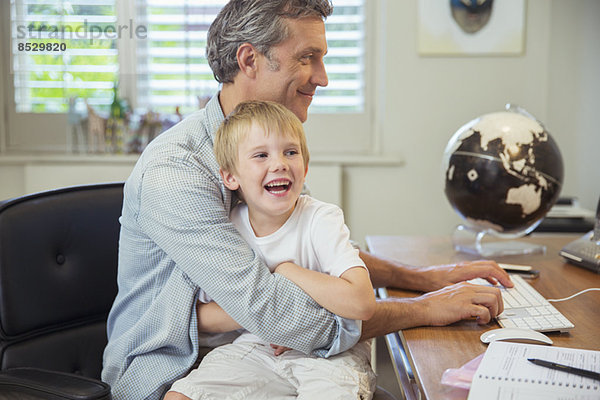 Vater hält Sohn und benutzt Computer