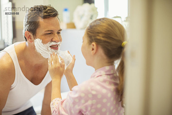 Mädchen reibt Rasiercreme auf Vaters Gesicht