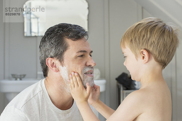 Junge reibt Rasierschaum auf Vaters Gesicht