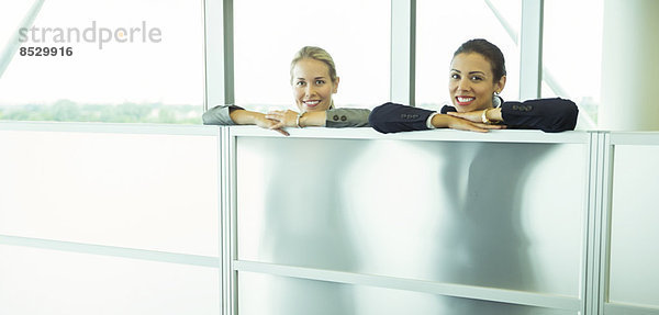 Lächelnde Geschäftsfrauen lehnen sich im Büro an die Halbwand