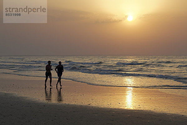 Zwei Männer laufen im Sonnenuntergang am Strand  Silhouette  Al-Batina Provinz  Oman  Arabische Halbinsel