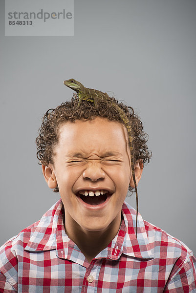 Ein Junge mit einer Eidechse  auf deren Kopf ein langer Schwanz krabbelt.