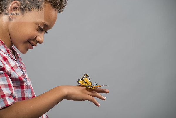 Ein Kind mit einem Schmetterling auf der Hand  der ganz still hält.