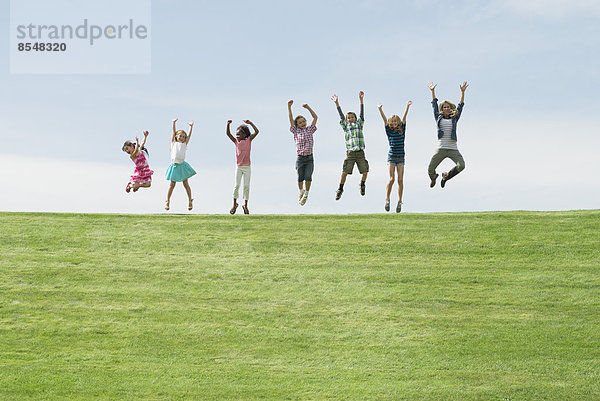 Eine Gruppe von Kindern auf dem Gipfel eines Hügels  die in einer Reihe in die Luft springen.