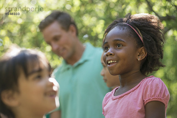 Eine Gruppe von Kindern und Erwachsenen im Schatten von Bäumen im Wald. Freunde und Familie gemeinsam im Freien.