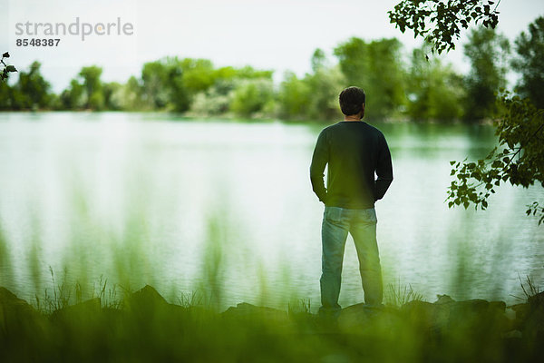 Ein Mann  der allein dasteht und tief in Gedanken in die Ferne über das Wasser schaut.