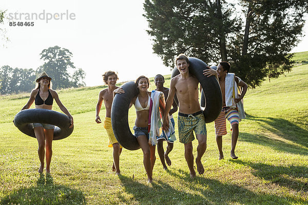 Eine Gruppe von Jugendlichen  Jungen und Mädchen  die Handtücher und Schwimmwagen halten und schwimmen gehen.