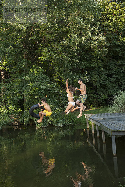 Drei kleine Jungen springen vom Steg in ein stilles Wasserbecken.