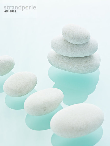 Glatte weiße Kieselsteine von einheitlicher Größe und Farbe auf einem blauen  reflektierenden Glashintergrund.