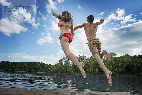 Zwei junge Menschen  ein Junge und ein Mädchen  rennen und springen vom Steg in einen See oder Fluss.