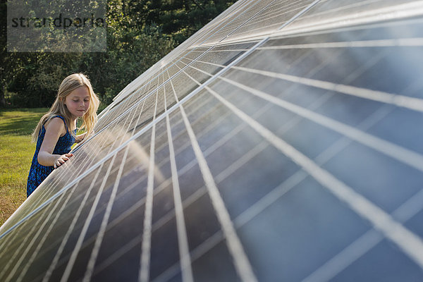 Ein junges Mädchen  das neben einer großen Solarzellenanlage steht und sich an sie lehnt.