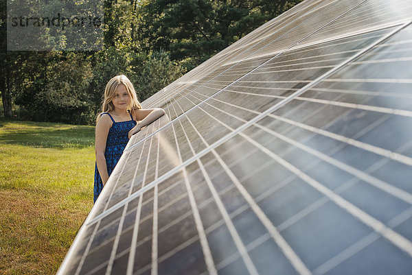 Ein junges Mädchen  das neben einer großen Solarzellenanlage steht und sich an sie lehnt.