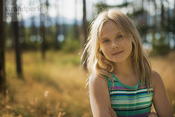 Ein Kind mit langen blonden Haaren im Wald an einem See.
