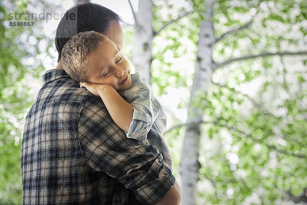 Ein Mann wiegt ein schlafendes Kind und ruht auf seiner Schulter.