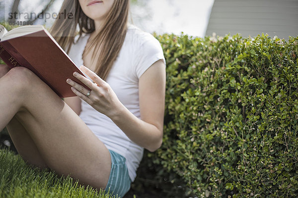 Ein Mädchen sitzt auf dem Rasen in einem Garten und liest ein Buch.