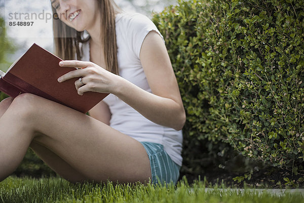 Ein Mädchen sitzt auf dem Rasen in einem Garten und liest ein Buch.