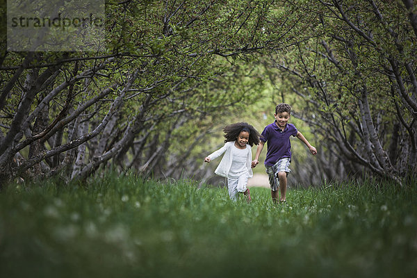 Zwei Kinder rennen durch einen natürlichen Asttunnel des Waldes.