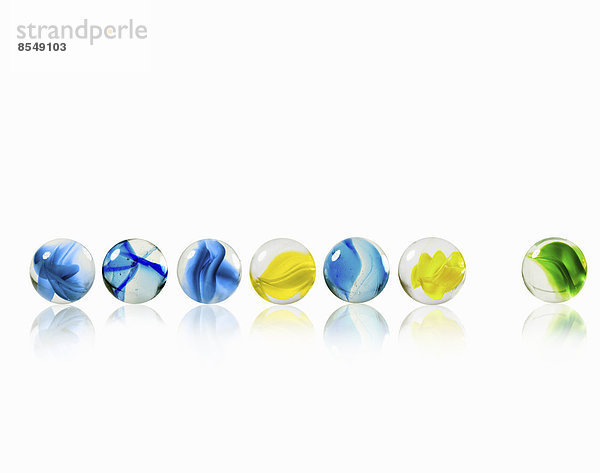 Eine Reihe von Glasmurmeln mit verschiedenen Mustern und Farben  von denen eine vom Rest getrennt ist.