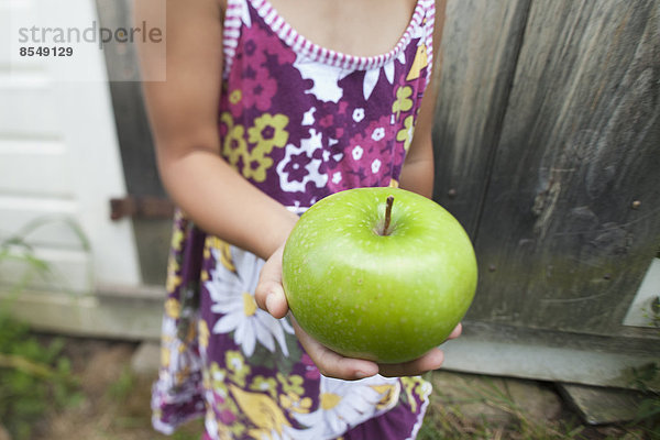 Ein Kind mit Zöpfen  das einen großen grünen Apfel kaut.