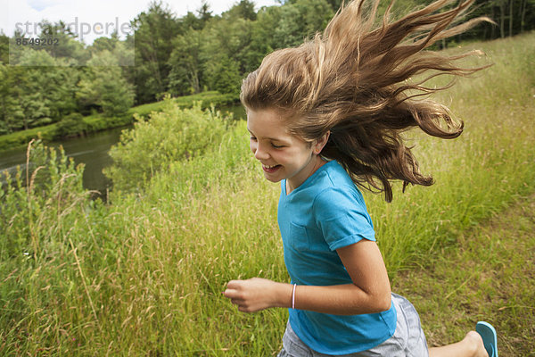 Ein junges Mädchen rennt auf einem Pfad an einem See entlang  die Haare fliegen ihr hinterher.
