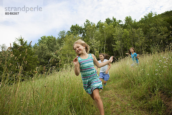 Drei Kinder  Mädchen spielen und lachen an der frischen Luft  jagen und rasen durch langes Gras.