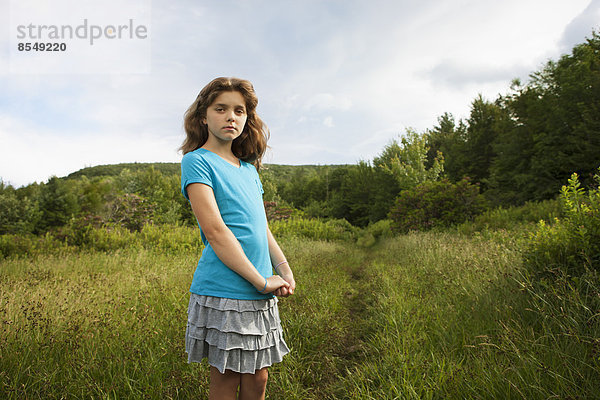Ein junges Mädchen steht an einem Weg durch das lange Gras in einem Feld.