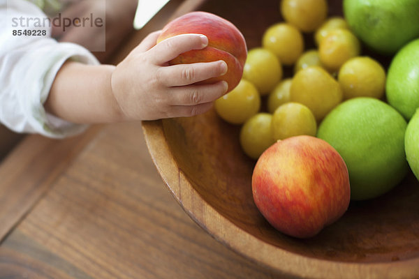 Ein kleines Kind  ein einjähriges Mädchen  das Früchte aus einer Schale greift.