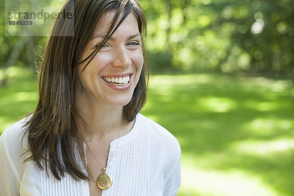 Eine Frau mit langen dunklen Haaren  die ein weißes Hemd trägt und lächelt.