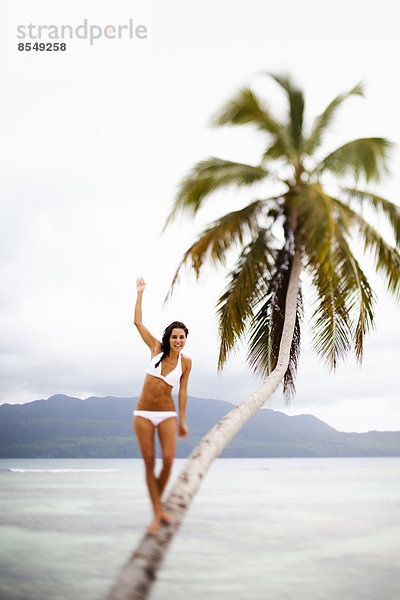 Eine Frau balanciert auf einer schiefen Palme in Las Galeras  Halbinsel Samana  Dominikanische Republik.