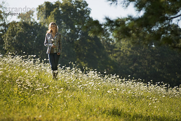 Eine junge Frau geht auf einer Wildblumenwiese spazieren.