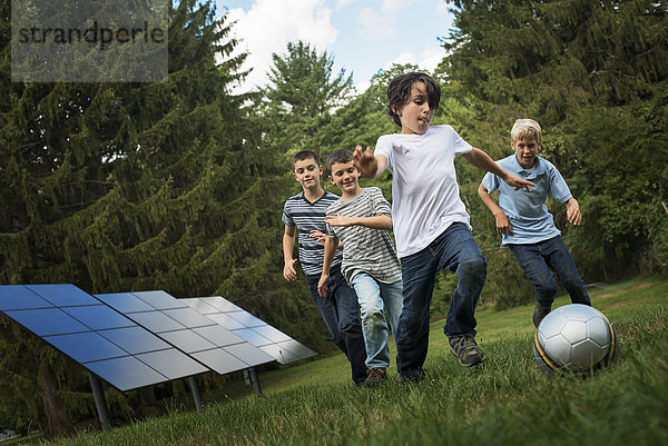 Eine Gruppe von Jungen rennt einem Ball hinterher  vorbei an Sonnenkollektoren im Wald.