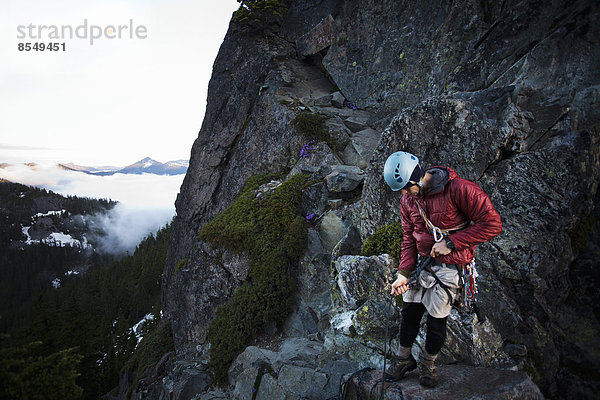Ein Felskletterer steht auf dem Gipfel eines Gipfels  nachdem er mit Hilfe eines Seils auf den Gipfel geklettert ist.