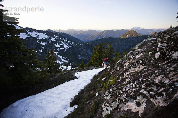 Ein junger Mann klettert um eine Schneefläche herum  während er auf den Gipfel eines großen Berges in den Cascades of Washington  USA  wandert.