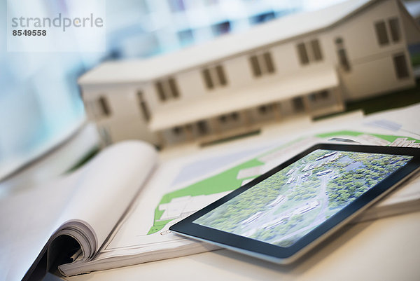 Ein Büro eines Architekturbüros. Ein Schreibtisch mit Blaupausen und Architekturplänen sowie ein Computertablett. Ein Architekturmodell eines Hauses.