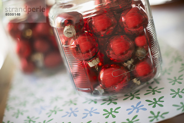 Roter Glaskugel-Weihnachtsschmuck in Glasgefäßen auf einer Tischplatte.