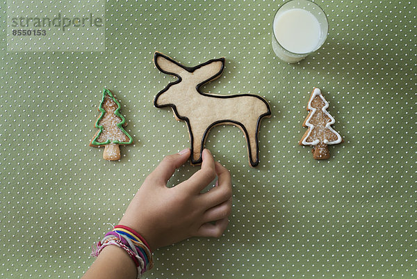 Die Hand eines Mädchens arrangiert ein selbstgebackenes Bio-Weihnachtsgebäck in Form eines Rentiers und von Weihnachtsbäumen.