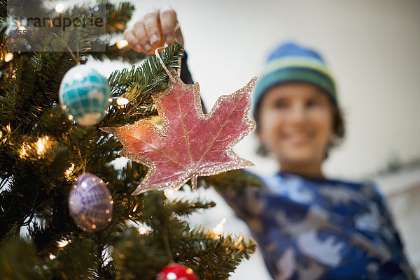 Ein kleiner Junge hält Weihnachtsschmuck in der Hand und legt ihn auf den Weihnachtsbaum.