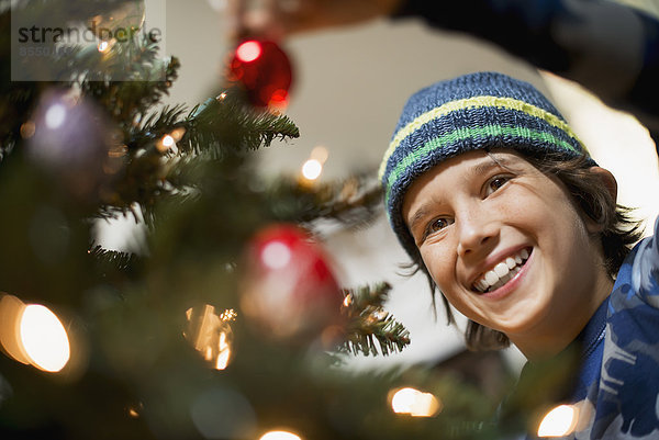 Ein kleiner Junge hält Weihnachtsschmuck in der Hand und legt ihn auf den Weihnachtsbaum.