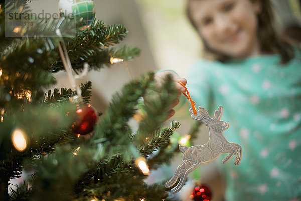 Ein junges Mädchen legt einen selbstgemachten Weihnachtsschmuck auf einen Baum.