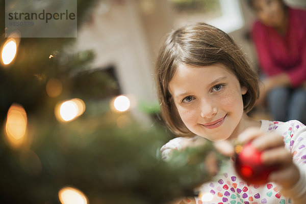 Ein Mädchen  das einen handgemachten Schmuck an einem Weihnachtsbaum platziert.